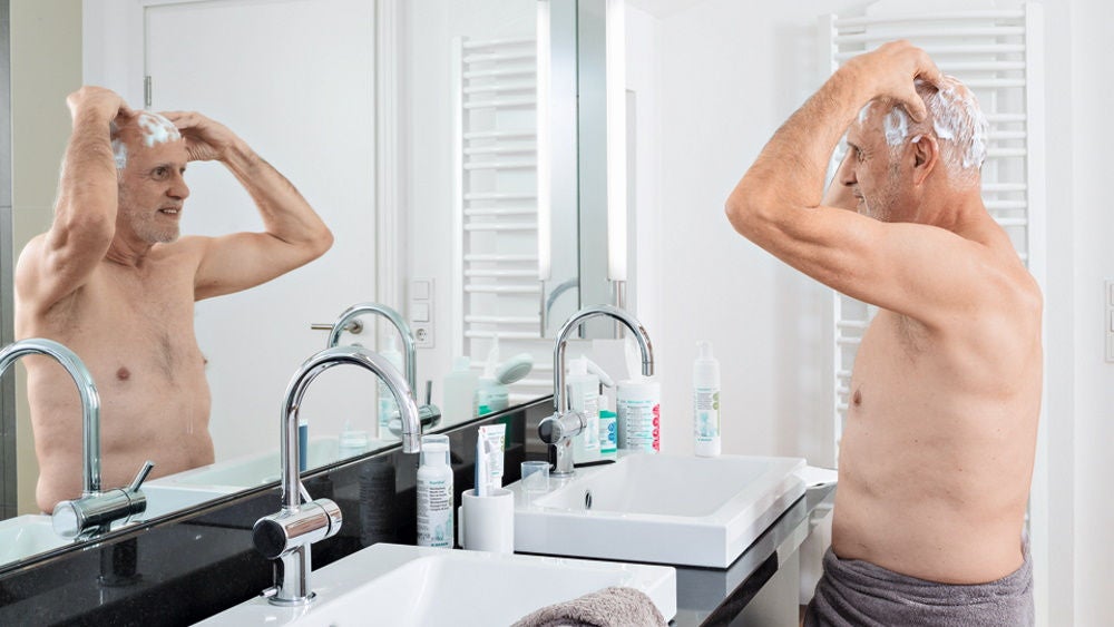 elderly man performing  antimicrobial hairwash at home in front of bath mirror 
