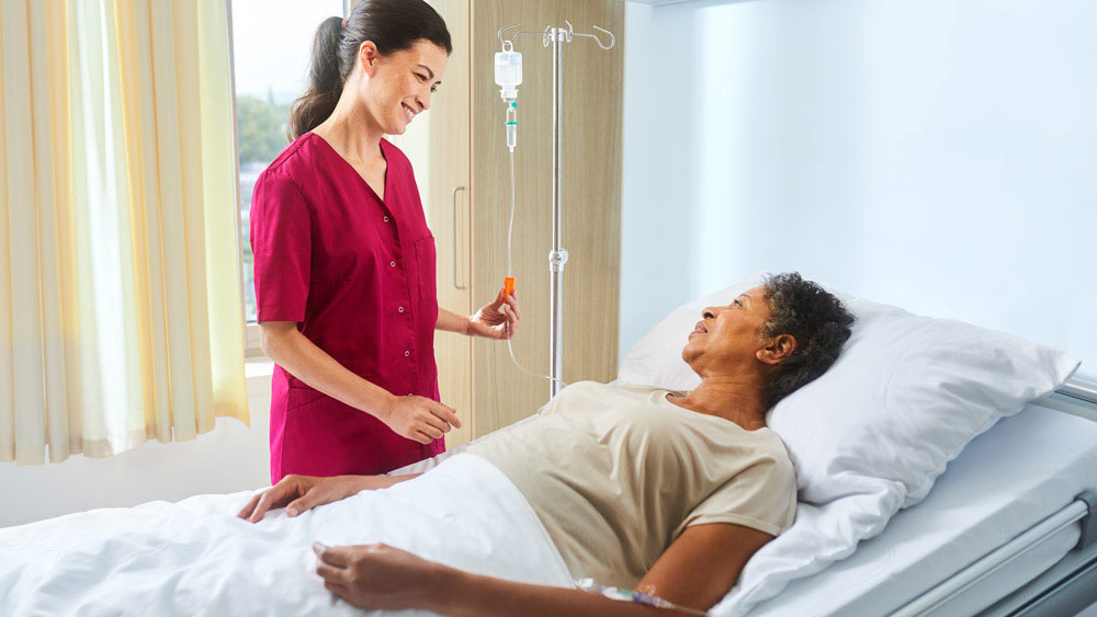 Infirmier avec ecoflac plus sur une potence à perfusion parlant à un patient allongé dans son lit