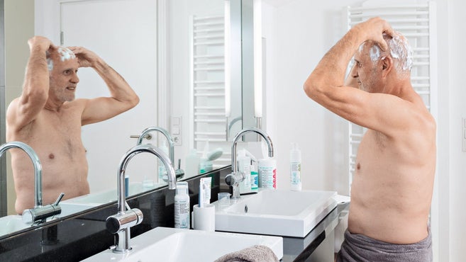oudere man doet thuis een antimicrobiële haarwas voor de badspiegel 