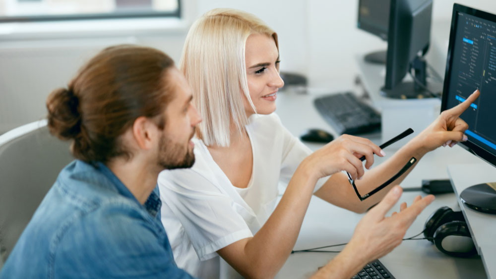 Twee zorgverleners zitten voor een computer. Ze toont hem iets op het scherm.